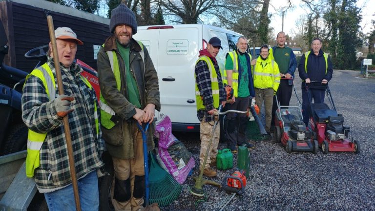 Image shows a group of people holding garden equipment outside